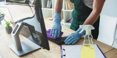 cropped shot of professional cleaner in rubber gloves cleaning computer keyboard in office